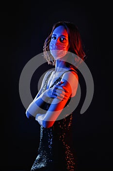 Beautiful young woman wearing a beaded mask on a black background. Mixed neon light