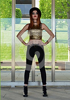 Beautiful young woman wearing black hat, gold top and black jeans modeling. Nineteen`s style. Fashion photo shoot.