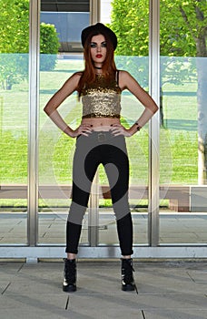 Beautiful young woman wearing black hat, gold top and black jeans modeling. Nineteen`s style. Fashion photo shoot.