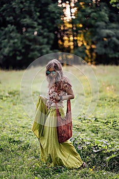 Beautiful young woman wearing bohostyle clothes posing in the rays of the evening sun, sunset. Boho style fashion