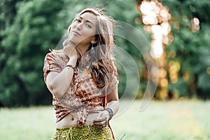 Beautiful young woman wearing bohostyle clothes posing in the rays of the evening sun, sunset. Boho style fashion photo