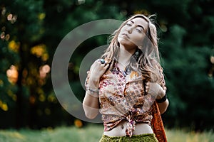 Beautiful young woman wearing bohostyle clothes posing in the rays of the evening sun, sunset. Boho style fashion photo