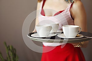 Beautiful young woman wearing bright clothes holding tray with coffee