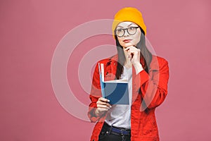 Beautiful young woman wearing casual and eyeglasses standing isolated over pink background, reading a book