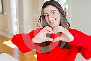 Beautiful young woman wearing casual red sweater smiling in love showing heart symbol and shape with hands