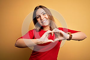Beautiful young woman wearing casual red t-shirt over yellow isolated background smiling in love showing heart symbol and shape