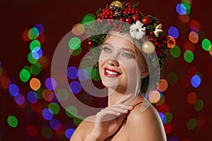 Beautiful young woman wearing Christmas wreath on blurred background