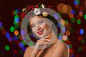 Beautiful young woman wearing Christmas wreath on blurred background