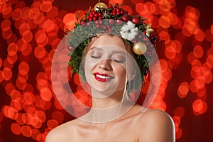 Beautiful young woman wearing Christmas wreath on blurred background