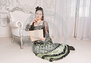 Beautiful young woman wearing green medieval vintage Victorian Style dress read letter on the floor