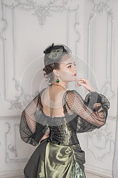 Beautiful young woman wearing green medieval vintage Victorian Style dress stand and turn in the room