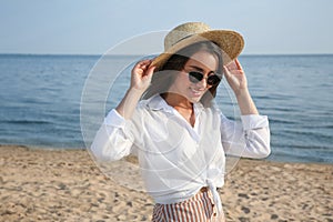 Beautiful young woman wearing hat and sunglasses on beach. Stylish headdress