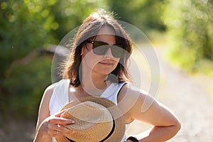 Beautiful young woman wearing hat and sunglasses walking on a country road