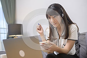Beautiful young woman wearing headset is making video conference call via computer at home