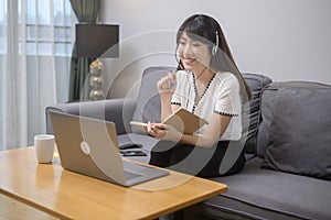 Beautiful young woman wearing headset is making video conference call via computer at home