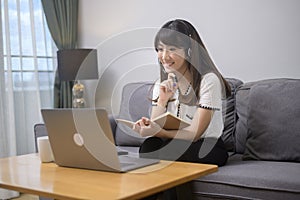 Beautiful young woman wearing headset is making video conference call via computer at home