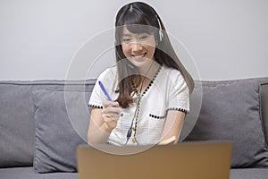 Beautiful young woman wearing headset is making video conference call via computer at home