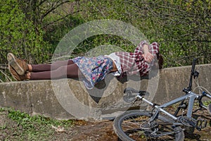 Beautiful young woman wearing helmet enjoying relax time after bike trip in forest. Lying near bike