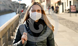Beautiful young woman wearing protective face mask walks along Navigli canals in Milan, Italy photo