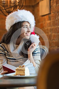 Beautiful young woman wearing Santa Claus red hat sitting at cafe