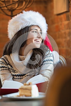 Beautiful young woman wearing Santa Claus red hat sitting at cafe