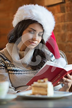 Beautiful young woman wearing Santa Claus red hat sitting at cafe