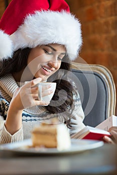 Beautiful young woman wearing Santa Claus red hat sitting at cafe