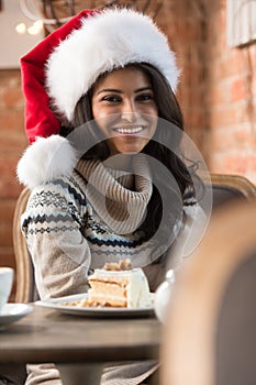 Beautiful young woman wearing Santa Claus red hat sitting at cafe