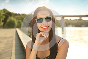 Beautiful young woman wearing stylish sunglasses near river