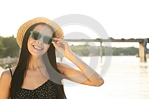 Beautiful young woman wearing stylish sunglasses near river. Space for text