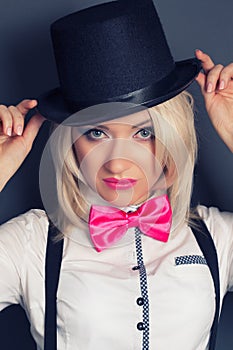 Beautiful young woman wearing tophat, bow-tie and braces against photo