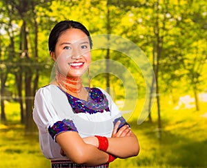 Beautiful young woman wearing traditional andean blouse with necklace, standing posing for camera, arms crossed smiling