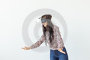 Beautiful young woman wearing virtual reality glasses and playing a game while standing against a white background with