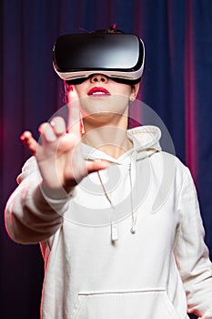 Beautiful young woman wearing virtual reality glasses and a white hoodie on a purple background. Modern technologies. Selective fo