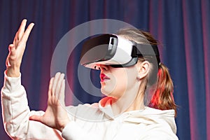 Beautiful young woman wearing virtual reality glasses and a white hoodie on a purple background. Modern technologies. Selective fo