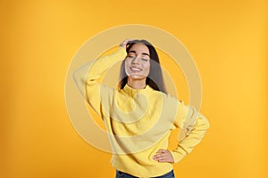 Beautiful young woman wearing warm sweater on yellow background