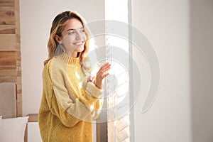 Beautiful young woman wearing warm yellow sweater near window at home