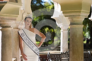 Beautiful young woman wearing a white dress and crown. The woman is the winner of a beauty contest and is having a photo shoot in