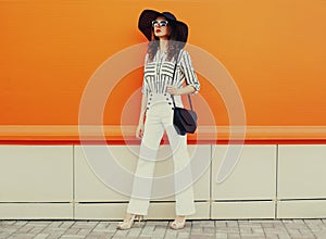 Beautiful young woman wearing a white striped shirt, black round hat on orange background