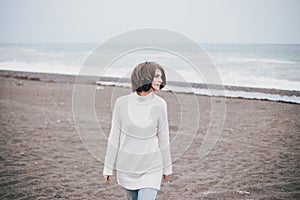 Beautiful young woman wearing white sweater and blue jeans walking on a lonely beach