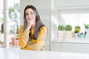 Beautiful young woman wearing yellow sweater looking confident at the camera with smile with crossed arms and hand raised on chin