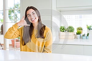 Beautiful young woman wearing yellow sweater smiling doing phone gesture with hand and fingers like talking on the telephone