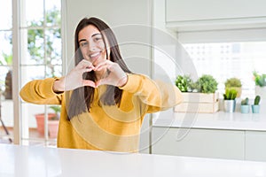 Beautiful young woman wearing yellow sweater smiling in love showing heart symbol and shape with hands