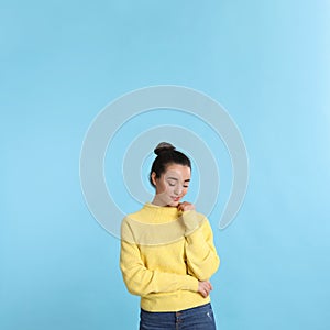 Beautiful young woman wearing yellow warm sweater on light blue background. Space for text