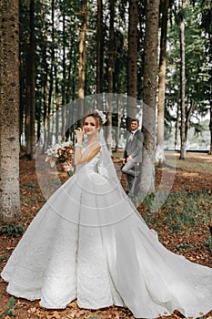 A beautiful young woman in a wedding dress between tall trees in the forest