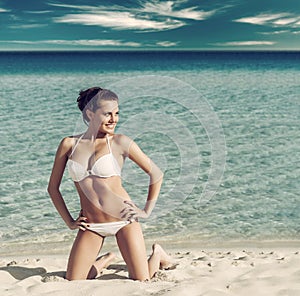 Beautiful young woman in white bikini posing on the beach near the sea