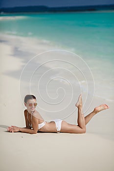 Beautiful young woman in a white bikini on a sandy tropical beach