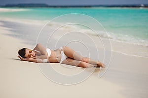 Beautiful young woman in a white bikini on a sandy tropical beach