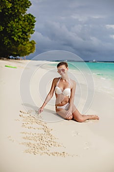 Beautiful young woman in a white bikini on a sandy tropical beach