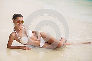 Beautiful young woman in a white bikini on a sandy tropical beach